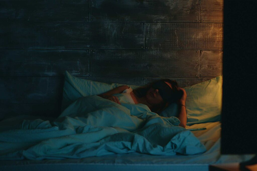 Frau liegt bei geringem Licht mit Schlafbrille im Bett