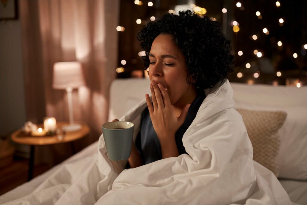 Eine gähnende Frau im Bett mit einer Tee-Tasse